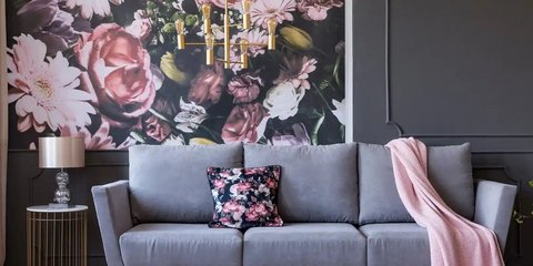 Graues Sofa mit Kissen, Blumenmuster-Tapete und dekorativen Elementen wie Lampen und Decken.